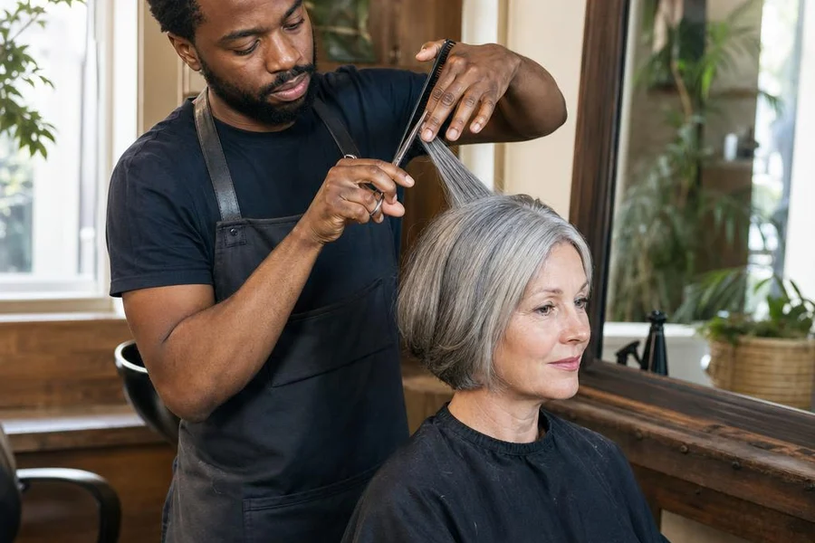 Een kapper knipt het zilvergrijze haar van een klant in een warme salon